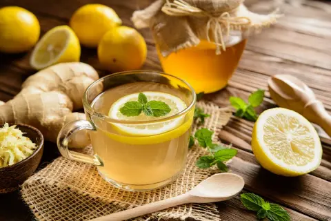 Une tasse de thé chaud au citron et à la menthe, avec du ginseng gingembre râpé, des citrons entiers et un pot de miel.