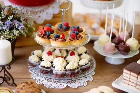 Słodkie przekąski: babeczki, tartaletki z owocami, cake pops i ciasto czekoladowe na drewnianym stole.