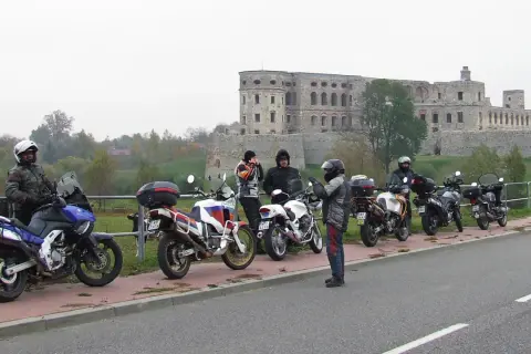 Motocykliści i ich maszyny na tle ruin zamku.