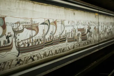 Detaljerad vy av Bayeuxtapeten på museum, med vikingaskepp och figurer som skildrar historiska händelser.