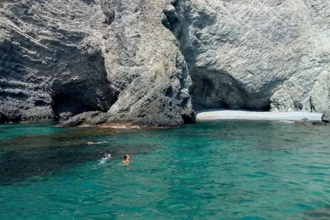 Gente nadando y haciendo snorkel en las aguas cristalinas de la cala puente Almería, rodeada de imponentes acantilados rocosos.