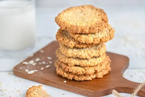 Ein Stapel goldbrauner schwedischer Haferkekse liegt auf einem Holzbrett, daneben ein Glas Milch.