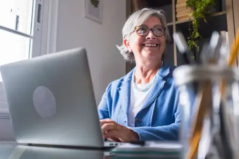 Lächelnde Frau am Laptop, die überlegt, wie sie Rente beziehen und vollzeit arbeiten kann, ohne die Steuerklasse zu ändern.