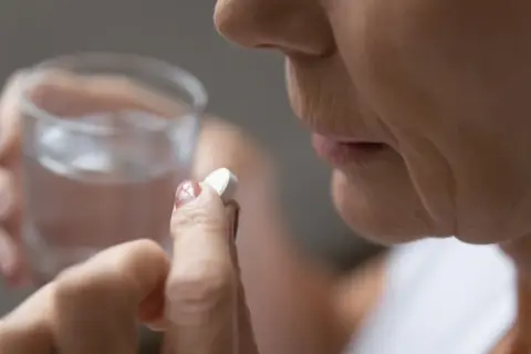 Dłoń trzyma tabletkę aspiryny i szklankę wody.
