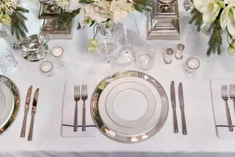 Elegant dukning med silverbestick på samma sida. Vita blommor och granris ger en festlig känsla.