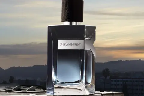 Elegancka butelka Y Yves Saint Laurent Y 100ml na tle zachodzącego słońca nad miastem.