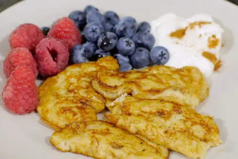En tallrik med gyllene pannkakor, färska hallon, blåbär och en klick yoghurt med kanel. Perfekt för diabetes mat recept.