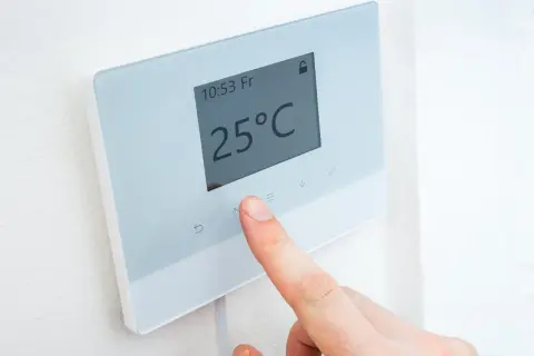 Un dedo ajusta la temperatura en un termostato digital que muestra 25°C.