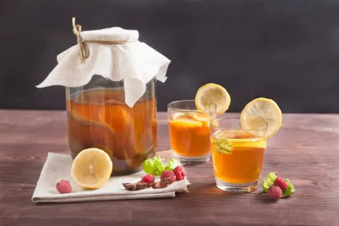 Un grand bocal de boisson kombucha, deux verres garnis de citron et de menthe, avec des framboises et une tranche de citron sur une serviette.