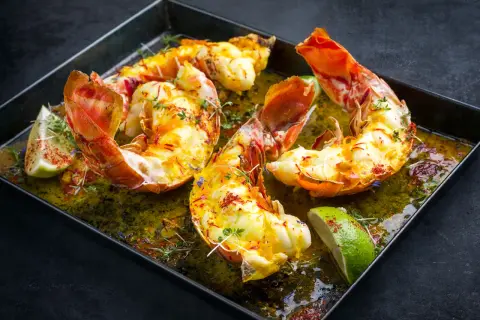 Langoustes grillées dans un plat avec du citron vert et des herbes.