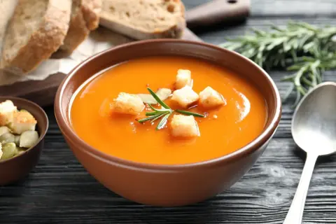 Aksamitny zupa krem z batatów, udekorowana grzankami i rozmarynem, podana z chlebem i pestkami dyni.