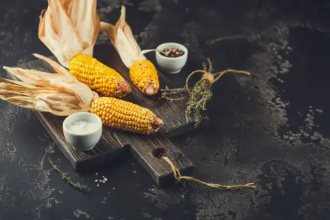 Kolby kukurydzy na desce, sól, pieprz i zioła. Czy kukurydza ma niski indeks glikemiczny?