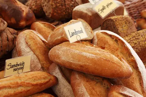 Różnorodne pieczywo, w tym bochenki z etykietami "Landbrood" i "Sandwich naturel". Zastanawiasz się, czym smarować chleb przed pieczeniem, by uzyskać chrupiącą skórkę?