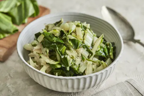Schüssel mit gedünstetem Mangold, perfekt für ein einfaches Mangold Rezept. Frische Blätter liegen daneben.