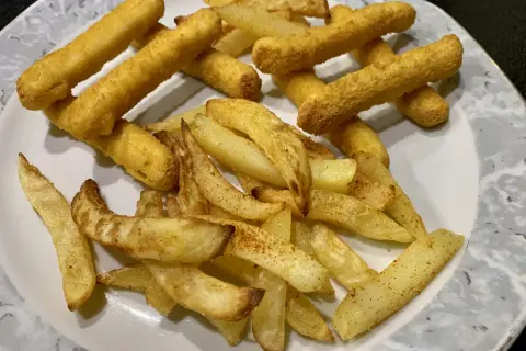 Ein Teller mit knusprigen belgischen Pommes, einige dick geschnitten, andere als Stäbchen frittiert.