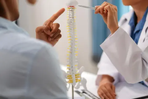 Lekarz pokazuje pacjentowi model kręgosłupa, wskazując na tylną wypuklinę krążka międzykręgowego.