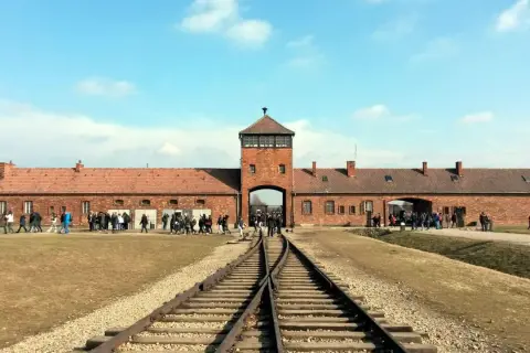 Brama obozowa Auschwitz I z wieżą, tory kolejowe prowadzące do niej. Zwiedzający zastanawiają się, ile trwa zwiedzanie Auschwitz, by poznać historię.