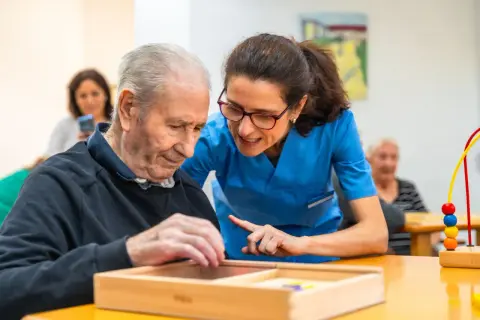 Un homme âgé participe à un atelier sensoriel, guidé par une aide-soignante attentive.