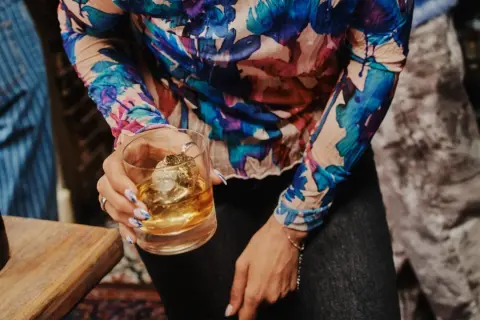 Kobieta trzyma szklankę z whisky Ballantine's. Zastanawia się, ile procent ma ten wyborny trunek.
