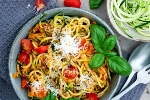 Herzhafte Zucchini-Nudeln mit Tomaten und Parmesan, garniert mit frischem Basilikum. Ein leichtes Gericht, das schmeckt.