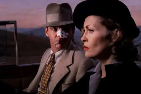 Jack Nicholson z plastrem na nosie i papierosem w ustach, obok Faye Dunaway w kapeluszu. Scena z jednego z filmów Romana Polańskiego.