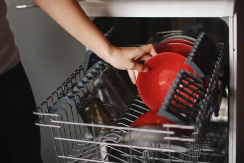 Ręka wkłada czerwony talerz do najlepszej zmywarki 45 cm wolnostojącej.