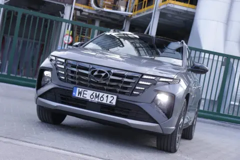 Nowoczesny Hyundai hybryda z charakterystycznym grillem i światłami LED, zaparkowany przy przemysłowym ogrodzeniu.