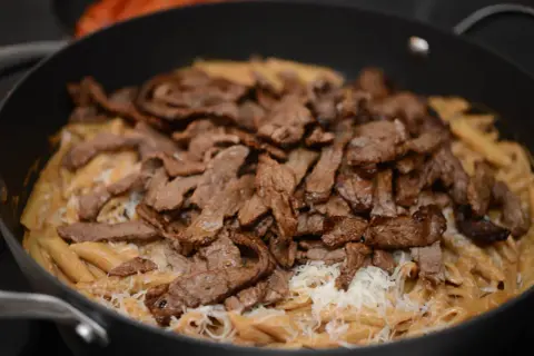En krämig pasta i ugn med strimlat kött och riven ost.