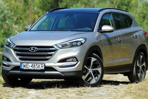 Srebrny Hyundai Tucson III na tle zieleni. Poznaj różne wersje wyposażenia tego wszechstronnego SUV-a.