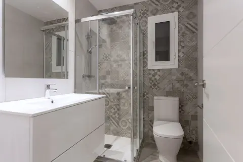 Salle de bain petite aux tons gris. Carrelage mural à motifs géométriques, douche vitrée, lavabo blanc et WC.
