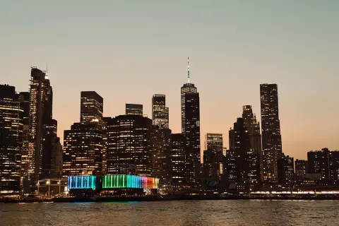 Wieczorny widok na Manhattan podczas zwiedzania Nowego Jorku. Podświetlone wieżowce odbijają się w wodzie.