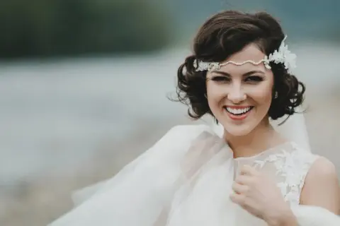 Novia sonriente con semirecogido pelo corto boda, diadema de perlas y encaje, velo vaporoso.