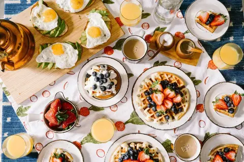 Un délicieux **heure du brunch dimanche** avec des gaufres aux fruits, des toasts à l'avocat et aux œufs, des fraises et du jus d'orange.