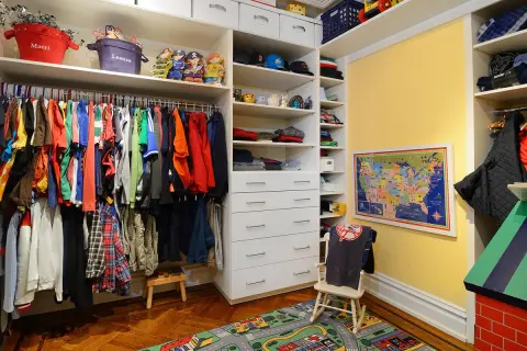 Armario infantil con ropa colgada en la barra, estantes con juguetes y cajones. La altura de la barra del armario es perfecta para los niños.