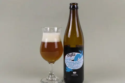 Szklanka z bursztynowym piwem i pianką obok butelki piwa typu new england ipa. Etykieta "Detka" z niebieskim motywem wodnym.
