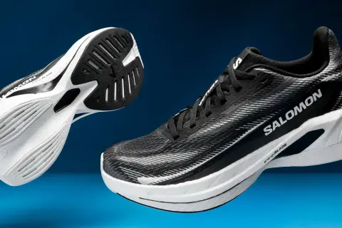 Deux chaussures de course Salomon Spectur noires et blanches, avec semelles blanches et noires, sur fond bleu.