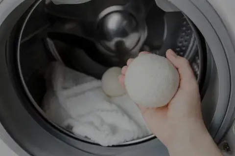 Mano che tiene una pallina per lavatrice, pronta per essere inserita nel cestello con il bucato. Scopri come si usa per un bucato più morbido.