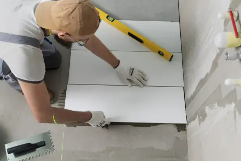 Pose d'un carrelage mural de salle de bain. Un carreleur utilise un niveau et un laser pour un calcul précis.