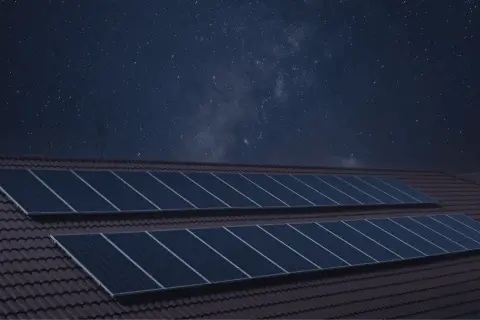 Paneles solares en un tejado bajo un cielo estrellado. La imagen sugiere que los paneles solares funcionan de noche, capturando la energía de las estrellas.
