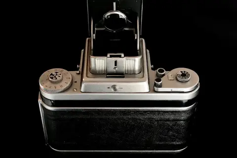 A vintage Pentacon Six camera, with its viewfinder open, sits on a reflective black surface.