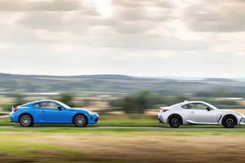 Dwa sportowe samochody, niebieska i srebrna Toyota 86, pędzą po wiejskiej drodze, tworząc dynamiczny obraz.