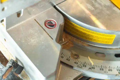 Detalle de una sierra ingletadora con marcas de ángulo para saber como medir para cortar a inglete. Se ve una advertencia de seguridad.