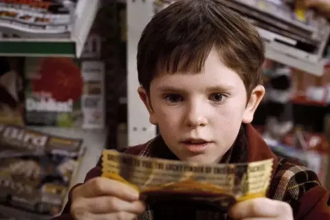 Chłopiec z filmu "Charlie i fabryka czekolady" trzyma złoty bilet. Freddie Highmore w tej roli to początek jego kariery w filmach, serialach i programach.