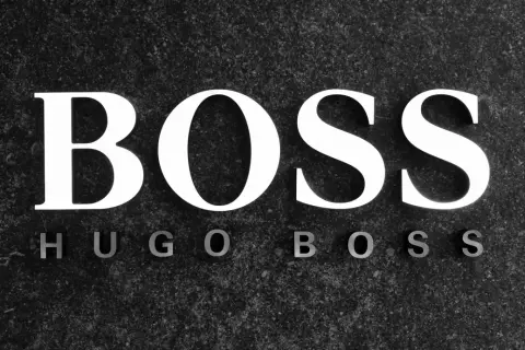 Białe litery "BOSS" na ciemnym, kamiennym tle. Poniżej mniejsze litery "HUGO BOSS". To symbol marki z bogatą historią.