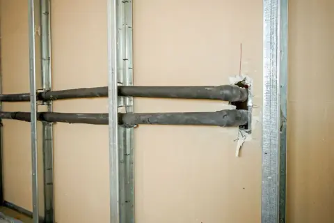 Instalacja hydrauliczna w trakcie budowy. Widoczne profile na ściankę działową i izolowane rury przechodzące przez otwory.