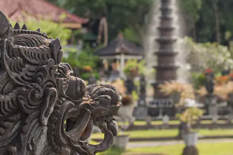 Eine detaillierte Steinskulptur eines Fabelwesens im Vordergrund, im Hintergrund ein Garten mit Brunnen und Pflanzen.