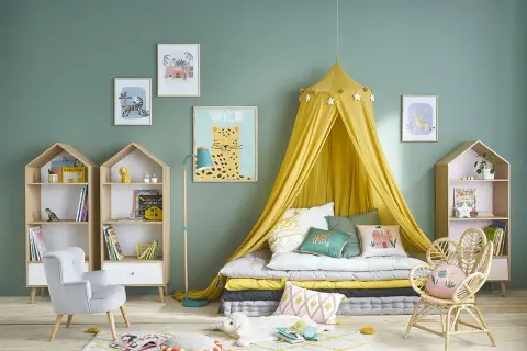 Chambre de fille tendance avec lit au sol, ciel de lit jaune, coussins animaux et étagères en forme de maison.
