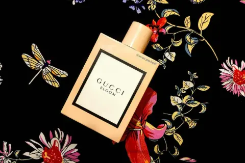 Elegancki flakon Gucci Bloom 100ml na tle kwiecistego wzoru z ważkami.