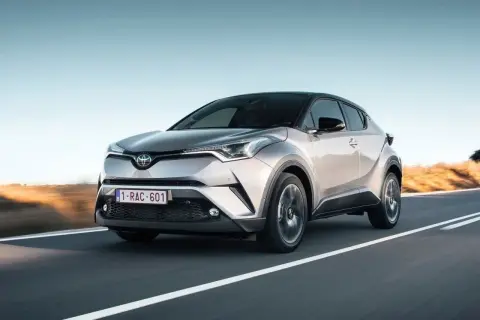Srebrna Toyota C-HR 2023 pędzi po pustej drodze, z zachodzącym słońcem w tle.