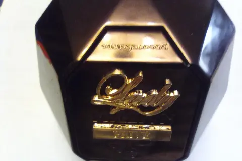 Złote logo "Lady" na ciemnym flakonie perfum, z napisem "Prive" poniżej. Elegancki dodatek dla każdej kobiety.